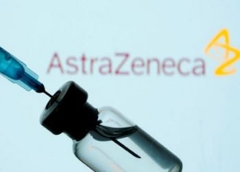 COVID-19 Vaccine - A vial and syringe are seen in front of a displayed AstraZeneca logo.